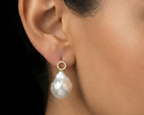 Woman wearing a gold hook earring with a large Keshi pearl and a diamond set circle