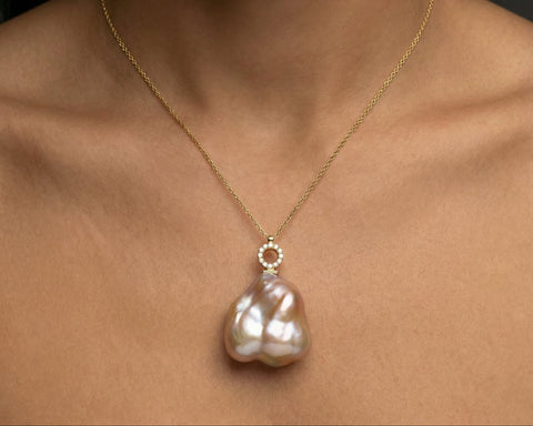 Gold necklace with a large pearl pendant on a person against a dark background