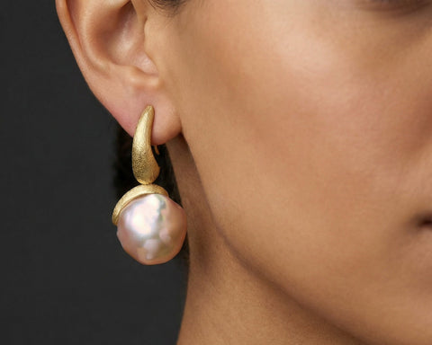 Gold earring with a pearl on an ear against a dark background