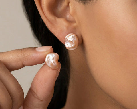 Close-up of a person wearing pearl earrings with one hand holding another pearl.