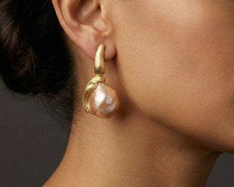 Close-up of a gold earring with a pearl on an ear against a neutral background