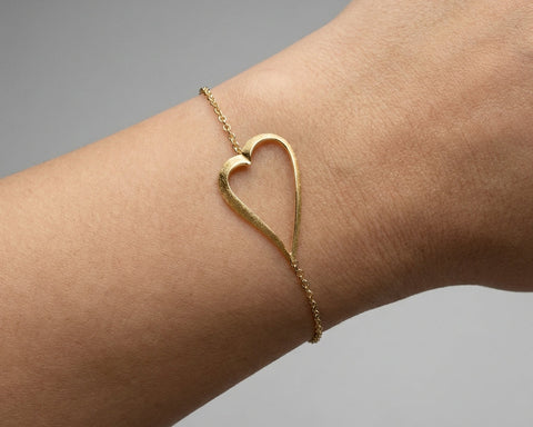 Gold heart-shaped bracelet on a wrist against a gray background