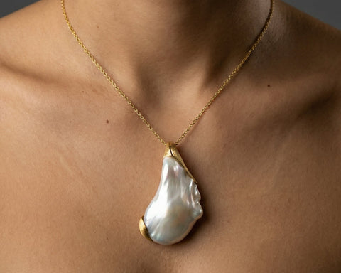 Gold necklace with a large pearl pendant on a person's neck