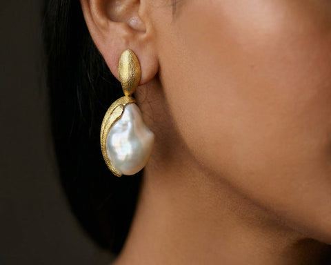 Gold earring with a pearl on a person's ear against a dark background