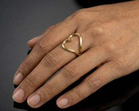 Hand wearing a gold heart-shaped ring on a dark background
