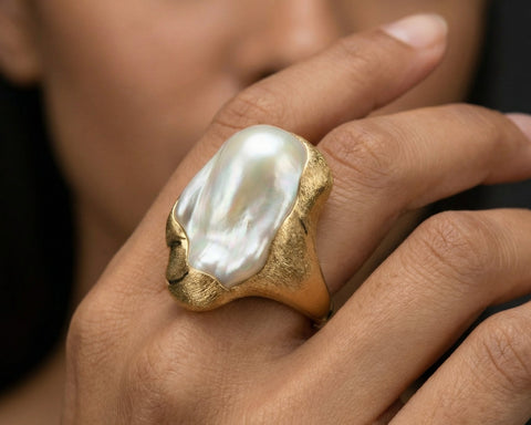 Gold ring with a large pearl on a person's finger