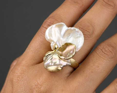 Gold and pearl ring on a hand against a dark background