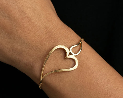 Gold heart-shaped bracelet on a wrist against a black background