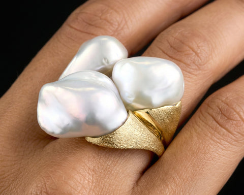 Gold ring with three large white pearls on a hand against a black background