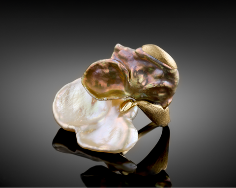 Gold and pearl ring on a reflective surface with a dark background