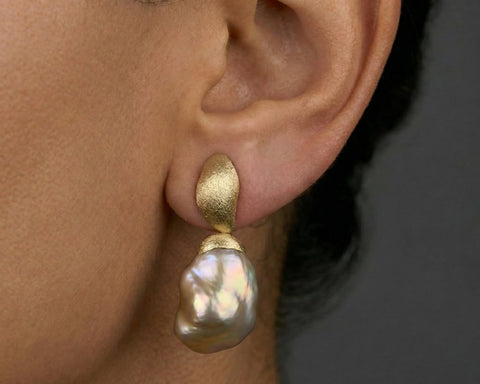 Gold earring with a pearl drop worn by a person against a dark background
