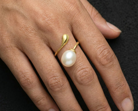 Gold ring with a pearl on a hand against a dark background