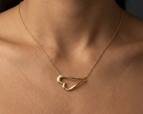 Gold necklace with a heart-shaped pendant on a person's neck against a dark background