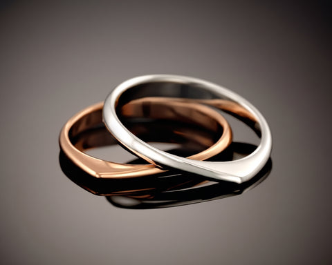 Two twisted rings, one rose plated and one silver, resting one inside the other