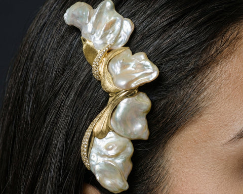 Pearl hair clip with gold accents on a person's head against a dark background