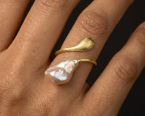 Gold ring with a large pearl on a hand against a black background