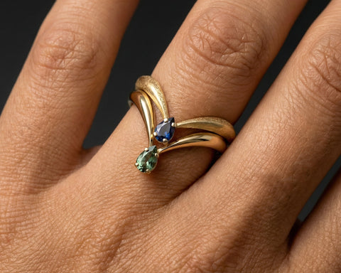 Gold ring with gemstones on a person's finger against a dark background