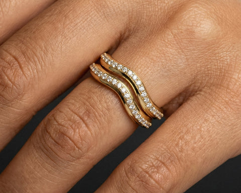 Gold ring with diamonds on a person's finger against a dark background