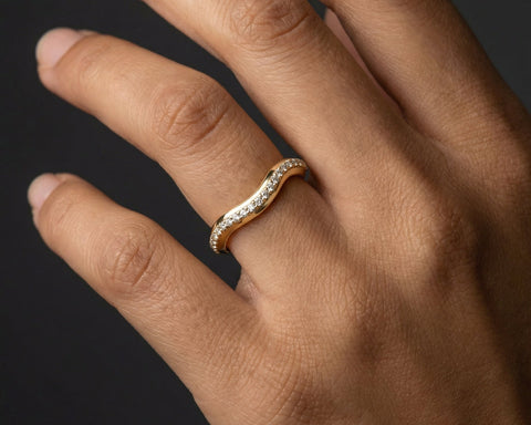 Hand wearing a gold ring with diamonds on a dark background