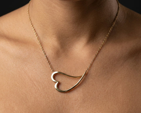 Gold heart-shaped necklace on a person's neck against a dark background
