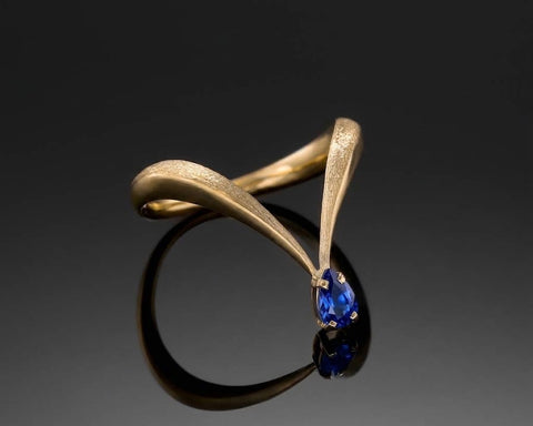 King Of Blue ring in yellow gold, a V shaped band with a pear-shaped blue sapphire at the tip