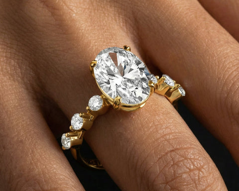 The oval solitaire in yellow gold worn on the hand, the stone running along the finger