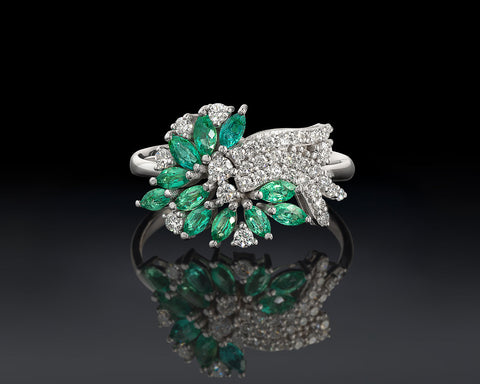Elegant ring with emerald green gemstones and silver accents on a reflective surface.