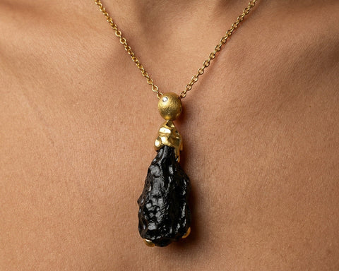 The black tektite pendant worn at the neckline on a 60 cm gold chain