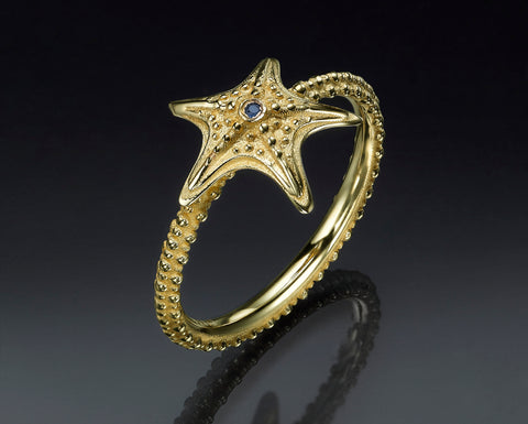 Starfish ring in 14K yellow gold with a blue sapphire, standing upright to show the arms falling over the band