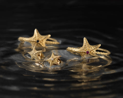 Starfish stud earrings in gold resting in shallow water