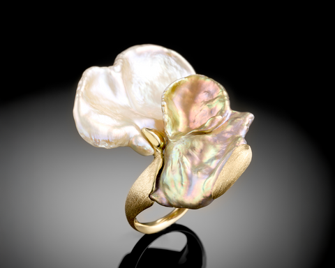 Gold ring with two large pearls on a reflective surface