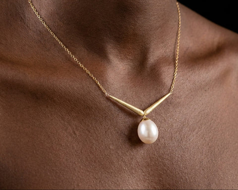 Gold V shaped necklace with a white oval pearl resting at the base of the throat