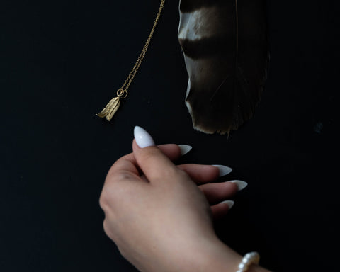 Gold feather held in the hand, showing the engraved texture