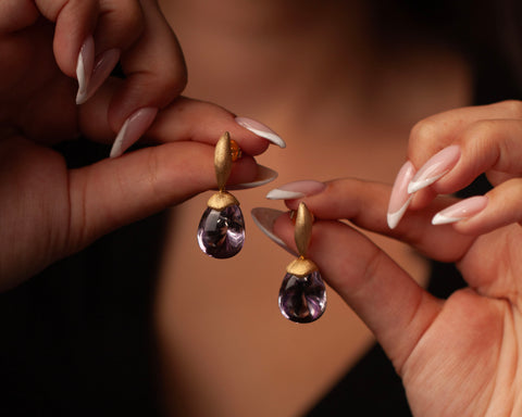 Woman holding a pair of gold and amethyst drop earrings