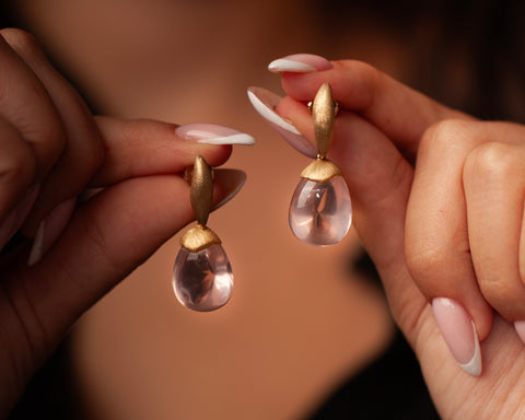 Woman holding a pair of gold and rose quartz drop earrings