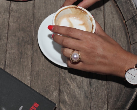 Woman wearing a gold floating pearl ring while holding a coffee cup