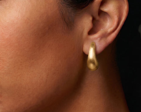 Brushed gold curved drop stud worn on the lobe