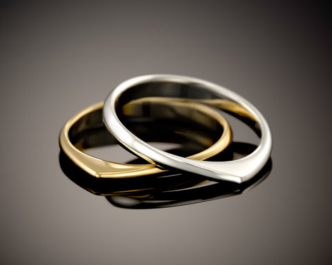 Two twisted rings, one gold plated and one silver, resting one inside the other