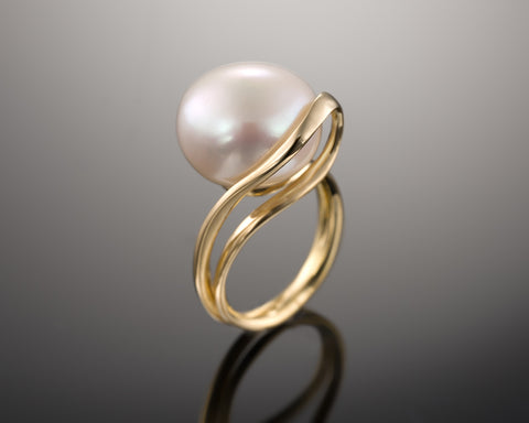Angled view of a yellow gold looping ring set with a white bouton pearl
