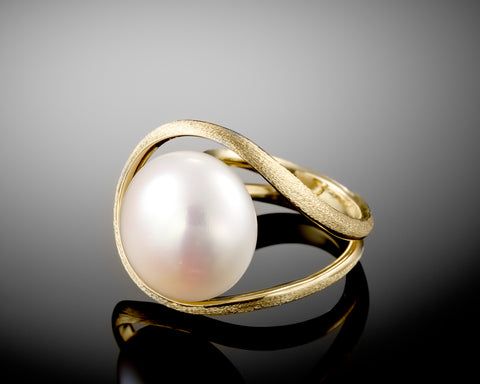 Side view of a gold open ring holding a large white bouton pearl from below